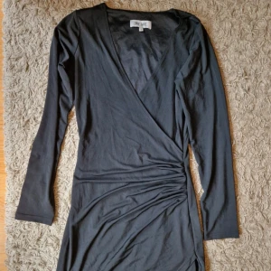 Svart omlottklänning från Dry Lake - Elegant svart omlottklänning från Dry Lake med långa ärmar och v-ringad design. Perfekt för en stilren look.