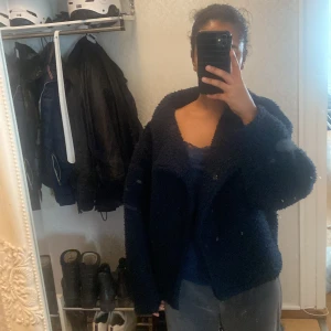 Mörkblå teddyjacka - Säljer en mysig mörkblå teddyjacka med en croppad passform. Jackan har långa ärmar och en hög krage som ger extra värme. Perfekt för kyliga dagar när du vill vara både bekväm och stilren.