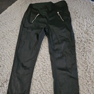 Oanvända byxor I skinnimitation  - Oanvända supersnygga byxor I skinnimitation med dragkedja I sidan och resår I midjan. Rak/smal modell. Fickor bak och fram . Nypris 599 kr . 98% bomull