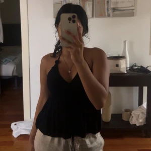 Svart ärmlös topp - Säljer en stilren svart ärmlös topp med smala axelband och v-ringning. Toppen har en lös passform och är perfekt för varma dagar. Köpt från BikBok för 250kr. 