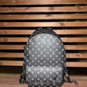 Lv ryggsäck  - Snygg svart ryggsäck från Louis Vuitton med det klassiska monogrammönstret i grått. Väskan har en praktisk dragkedja och justerbara axelremmar. Perfekt för att bära dina saker med stil.