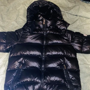 Svart pufferjacka från Moncler - Säljer en snygg svart pufferjacka från Moncler. Jackan har en glansig finish med dragkedja framtill och en huva för extra värme. Perfekt för kyliga dagar och har Monclers ikoniska logga på ärmen. Ett måste för garderoben! Taggen funkar. PRIS kan diskuteras!