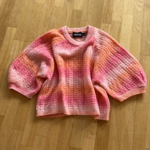 Färgglad stickad tröja från Pieces - Säljer en mysig stickad tröja från Pieces i härliga nyanser av rosa och orange. Tröjan har ett vågigt mönster och trekvartsärmar, perfekt för en färgglad look. Passar bra till både jeans och kjol!