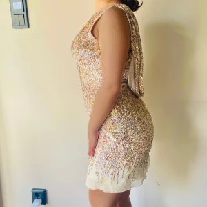 Glittrig Terani couture paljettklänning - Säljer en Terani couture  klänning med paljetter i guld och rosa. Klänningen har en djup v-ringad rygg och är ärmlös. Perfekt för en festlig kväll!