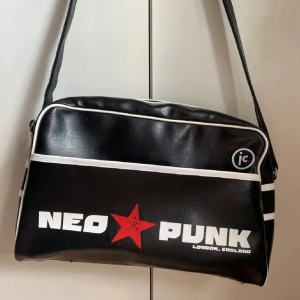 Svart axelväska med Neo Punk-tryck - Cool svart axelväska med Neo Punk-tryck i vitt och en röd stjärna. Väskan har vita detaljer och en justerbar axelrem. I fint skick! Rymlig då den får plats med dator och mera🌟
