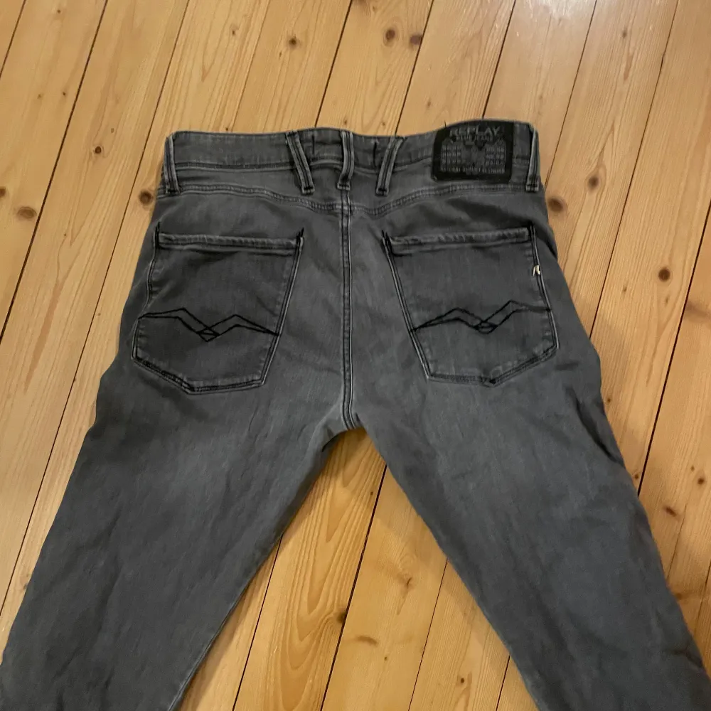 Snygga grå Replay Anbass jeans med en klassisk femficksdesign. De har en dragkedja och knapp framtill samt stilrena bakfickor med diskret broderi. Perfekta för en avslappnad look.. Farkut & Housut.