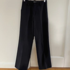 Svarta byxor från Lindex - Snygga svarta byxor från Lindex i storlek 152. Tillverkade av 90% polyester och 10% elastan för en bekväm passform. Perfekta för en stilren look. De har även en justerbar midja. 