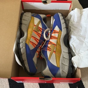 Nike Air Humara '17 QS - Säljer ett par Nike Air Humara '17 QS sneakers i en cool färgkombination av blå, orange och beige. Skorna har en robust sula och snörning i orange för en sportig look. Perfekta för utomhusaktiviteter.