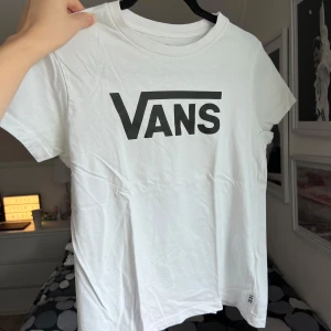 Vit t-shirt från Vans - Säljer en klassisk vit t-shirt från Vans med deras ikoniska logga i svart på bröstet. Perfekt för en avslappnad stil. T-shirten har en rund hals och korta ärmar. Storlek M, passar mig som har S. Axel: 38cm. Längd: 52cm.