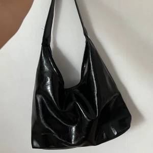 Svart handväska i fejkläder - Snygg svart axelväska i glansigt fejkläder. Aldrig använd.