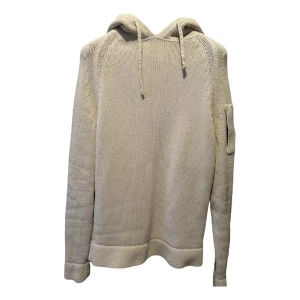Beige stickad hoodie från C.P. Company - Säljer en snygg beige stickad hoodie från C.P. Company. Tröjan har en huva med dragsko och en cool detalj på ärmen. Perfekt för en stilren och avslappnad look.