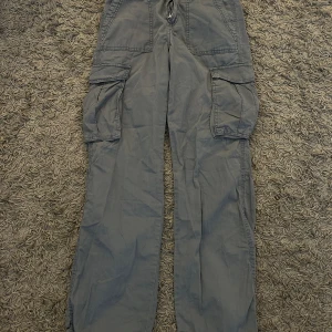 Grå cargobyxor med fickor - Säljer ett par grå cargobyxor med stora fickor på sidorna och baktill. Byxorna har en loose passform.