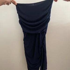 Mörkblå klänning - Elegant mörkblå klänning med draperad design. Perfekt för en stilren look. Klänningen har en smickrande passform och är tillverkad i ett mjukt material.