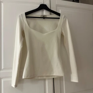 Vit långärmad topp - Säljer en stilren vit långärmad topp med v-ringning. Perfekt för en elegant och enkel look. Toppen har en figurnära passform och är tillverkad i ett mjukt material.
