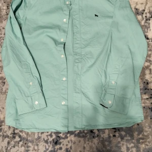 Grön skjorta med broderad detalj - Snygg ljusgrön skjorta från Ralph Lauren med en liten broderad logga på bröstet. Skjortan har långa ärmar och knappar framtill. Perfekt för en stilren look.