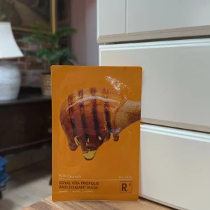 Royal Vita Propolis Anti-Oxidant Mask - En lyxig ansiktsmask med propolis och antioxidanter från Dr. Ceuracle. Perfekt för att ge huden en strålande och återfuktad känsla. Masken kommer i en gyllene förpackning med en bild av honung på framsidan.