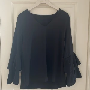 Svart blus med volangärmar från Gina Tricot - Svart blus från Gina Tricot med v-ringning och långa volangärmar. Perfekt för en stilren look. 💕