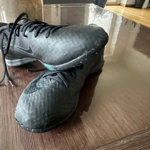 Svarta Nike fotbollsskor - Säljer ett par svarta Nike fotbollsskor med snörning och en diskret Nike-logga. Skorna har en mönstrad sula för bra grepp på planen. Perfekta för fotbollsträning och matcher.