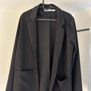 Svart kavaj - Snygg svart kavaj med normal passform och långa ärmar. Den har en klassisk design med två fickor framtill. Kavajen är från Lager 157 och är använd 1 gång 