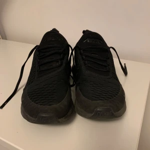 Svarta Nike sneakers - Säljer ett par svarta Nike sneakers med snörning och en stilren design. Skorna har en robust sula och är perfekta för vardagsbruk. De är märkta med 'Air' på baksidan och har en sportig look.