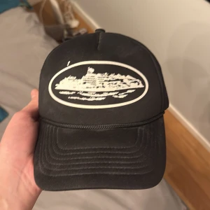 Svart corteiz  - Snygg svart keps med ett vitt tryck av en båt på framsidan. Kepsen har ett nätmaterial på sidorna för bättre ventilation. Perfekt för en avslappnad stil.