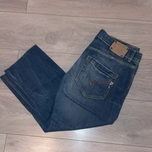 Blå jeans från Dondup - Säljer ett par snygga blå jeans från Dondup i modellen John. De är tillverkade i 100% bomull och har en klassisk design med tydliga sömmar. De är i bra skick och är perfekta för hösten nu när det blir lite kallare