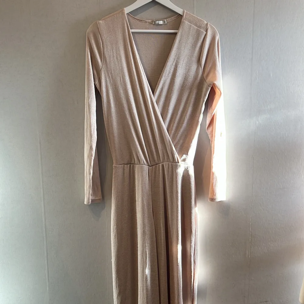 Säljer en elegant champagnefärgad jumpsuit. Den har långa ärmar och en v-ringad hals, perfekt för festliga tillfällen. Materialet ser ut att vara mjukt och bekvämt, vilket gör den både stilren och skön att bära. Använd 2 gånger. . Klänningar.