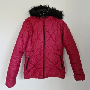 Rosa pufferjacka med fuskpäls - Säljer en rosa quiltad jacka i storlek 34. Den har en mysig huva med svart fuskpäls och praktiska fickor med knappar. Finns en liten vit fläck vid ena fickan som definitivt går bort i tvätt, i övrigt som ny. Perfekt för en vintrig y2k-stil!
