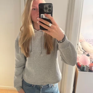 Grå croppad hoodie - Säljer en supermysig grå croppad hoodie. Perfekt för chill dagar eller när du vill ha en avslappnad stil. Den har en klassisk huva med dragsko och långa ärmar. Passar perfekt till jeans eller leggings!