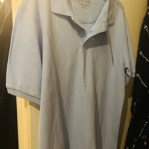 Ljusblå pikétröja från Nautica - Säljer en ljusblå pikétröja från Nautica, perfekt för en stilren och avslappnad look. Tröjan är i nyskick och har en klassisk krage med knappar. Den är gjord i ett bekvämt material som passar bra till både vardag och lite finare tillfällen.