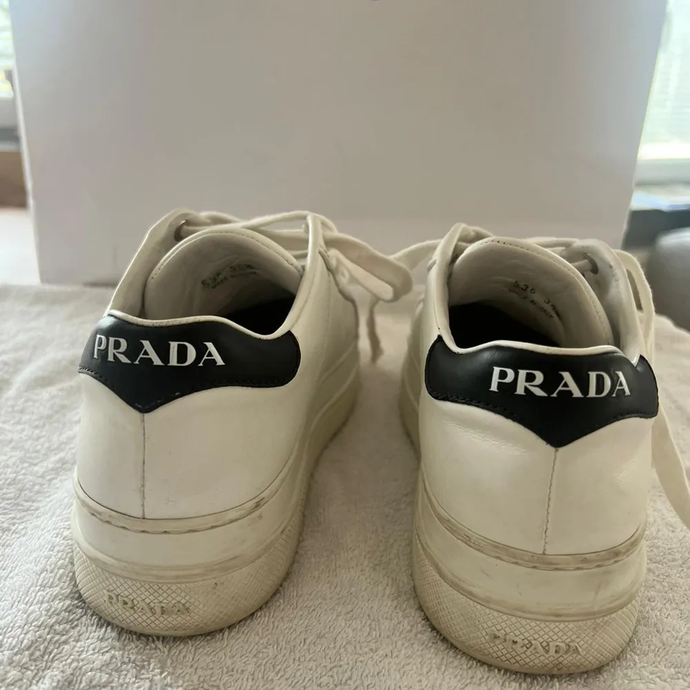 Säljer ett par stilrena vita sneakers från Prada i storlek 36. Skorna är tillverkade i Italien och har en klassisk design med snörning och en diskret logga på hälen. De är i bra skick och perfekta för både vardag och fest. Passar till alla säsonger och ger en lyxig touch till din outfit.. Skor.