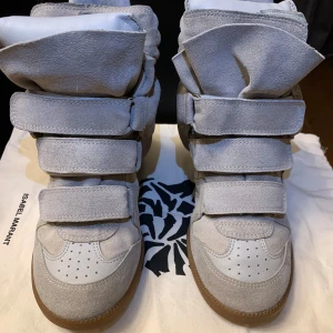 Grå sneakers från Isabel Marant - Snygga grå sneakers från Isabel Marant med flera kardborreband och en unik design. Skorna har en högre siluett och är tillverkade i mocka med en gummisula. Perfekta för en trendig look.