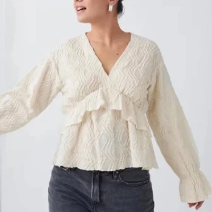 Vit omlottblus med volangdetaljer - Säljer en stilren vit omlottblus med v-ringning och volangdetaljer. Blusen har långa ärmar och ett subtilt mönster som ger en elegant touch.  Skriv för fler bilder,pris går att diskutera.