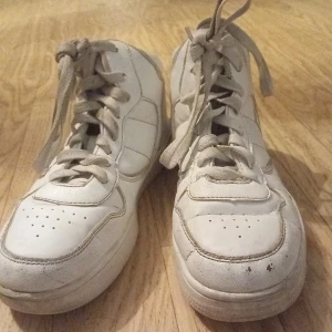 Vita sneakers med snörning - Säljer ett par vita sneakers med snörning. Skorna har en klassisk design med perforerade detaljer på tån och en högre ankel. Perfekta för en avslappnad stil.