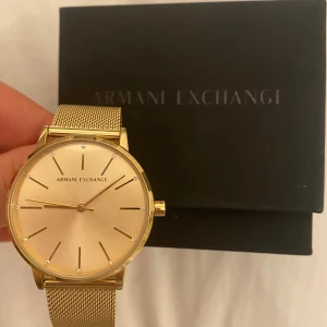 Guldfärgad klocka från Armani Exchange - Elegant guldfärgad klocka från Armani Exchange med en stilren urtavla och mesharmband. Perfekt för att ge en lyxig touch till din stil. Använt den endast ett tillfälle. Ljusterbar. 