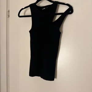 Svart ribbad linnetopp från BikBok - Snygg svart ribbad linnetopp från Zara. Perfekt för en stilren look med sin ärmlösa design och tight passform. Ny med tagg kvar.