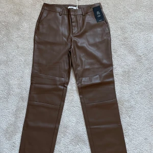 Bruna skinnbyxor från NA-KD oanvänd 40 - Snygga bruna skinnbyxor från NA-KD med en stilren design. Byxorna har en rak passform och är högmidjade, vilket ger en modern look. Perfekta för att lyfta vilken outfit som helst.