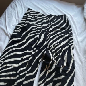 Zebramönstrade byxor från H&M - Snygga zebramönstrade byxor från H&M i svart och vitt. Byxorna har en loose passform och är perfekta för en trendig look. De är tillverkade i ett mjukt och bekvämt material med elastisk midja för extra komfort.