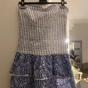 Blåvit mönstrad klänning - Axelbandslös klänning i blått och vitt med ett fint mönster. Använd endaste 1 gång och är som ny. Passar på mig om är xs/s 