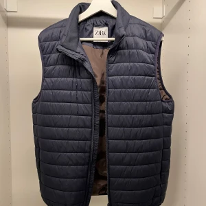 Mörkblå quiltad väst från Zara - Snygg mörkblå quiltad väst från Zara med dragkedja. Perfekt för lager-på-lager under kyliga dagar. Stilren design som passar till många outfits.