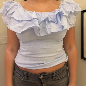 Ljusblå offshoulder topp med volang - Säljer en söt ljusblå offshoulder topp med volangdetaljer. Toppen har en tight passform och är perfekt för sommardagar. Den är tillverkad i ett mjukt och bekvämt material. Skit snygg fest topp