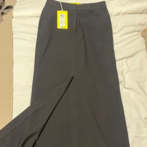 Svart långkjol - Elegant svart långkjol med en stilren design. Kjolen har en diskret slits framtill och är perfekt för en sofistikerad look. Passar utmärkt till både vardag och mer formella tillfällen.