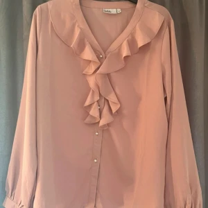 Rosa blus med volanger - Jätte bra skick. ”Knapparna” är vita pärlor. Säljer då jag inte passar i färgen. Storlek M men passar mer som en S.