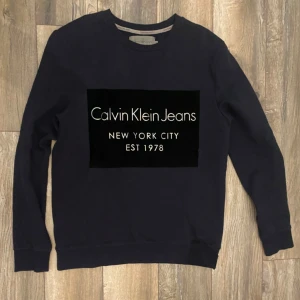 Svart tröja från Calvin Klein Jeans - Snygg svart tröja från Calvin Klein Jeans med tryck på bröstet. Perfekt för en stilren look. Tröjan har långa ärmar och rund halsringning.