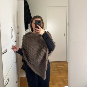 Äkta pälsponcho - Säljer denna poncho i äkta päls i en snygg ljusbrun färg. Aldrig använd!!