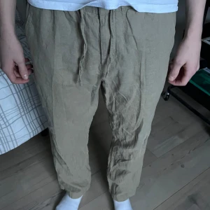 Beige linnebyxor från H&M - Säljer ett par bekväma beige linnebyxor från H&M med snörning i midjan. Byxorna har en avslappnad passform och är perfekta för varma dagar. De är tillverkade i ett lätt och luftigt material.