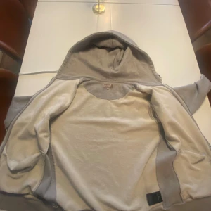 Grå hoodie från Morris - Säljer en stilren grå hoodie från Morris med dragkedja och justerbar huva. Perfekt för en avslappnad look. Tröjan har långa ärmar och en liten logotypdetalj på bröstet.