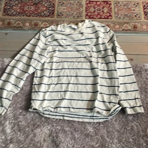 Vit och blå randig långärmad tröja - Säljer en stilren vit tröja med blå ränder. Tröjan har långa ärmar och en avslappnad passform, perfekt för en casual look. Passar bra till jeans eller chinos.