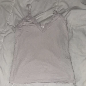 Vit ribbad linnetopp med spetsdetaljer - Säljer en stilren vit  ribbad linnetopp med v-ringad spetskant. Perfekt för lager-på-lager eller som den är. Justerbara axelband för bästa passform.