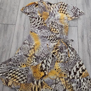 Klänning - Snygg mönstrad klänning från Shein i olika djurmönster och geometriska former. Klänningen har en omlott-design med knytband i midjan och korta ärmar och massor av volanger! Perfekt för en unik och trendig stil. Storlek S💋🐆🐅 Som nytt skick